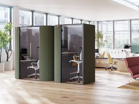 A side-by-side view of Bay Work Pod and Bay Work Pod Pro with workstations in the background and lounge setting off to the right. A side-by-side view of Bay Work Pod and Bay Work Pod Pro with workstations in the background and lounge setting off to the right.