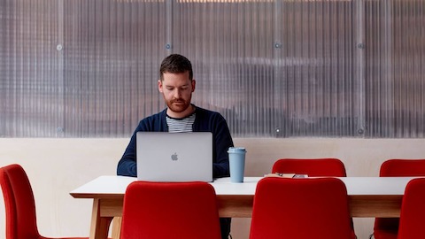 A man working on a laptop at a white Dalby table with 8 red Viv chairs around the table. A man working on a laptop at a white Dalby table with 8 red Viv chairs around the table.