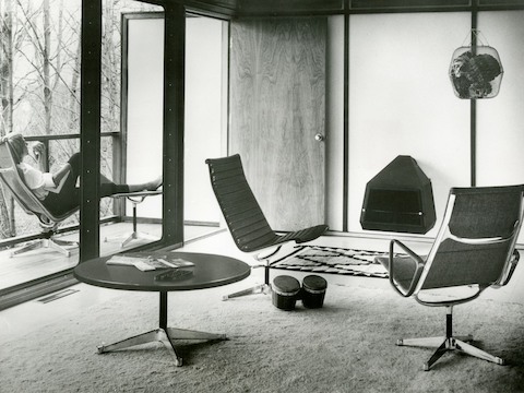 Black Eames Aluminum Group lounge chairs and a round Eames occasional table in a residential setting. Black Eames Aluminum Group lounge chairs and a round Eames occasional table in a residential setting.