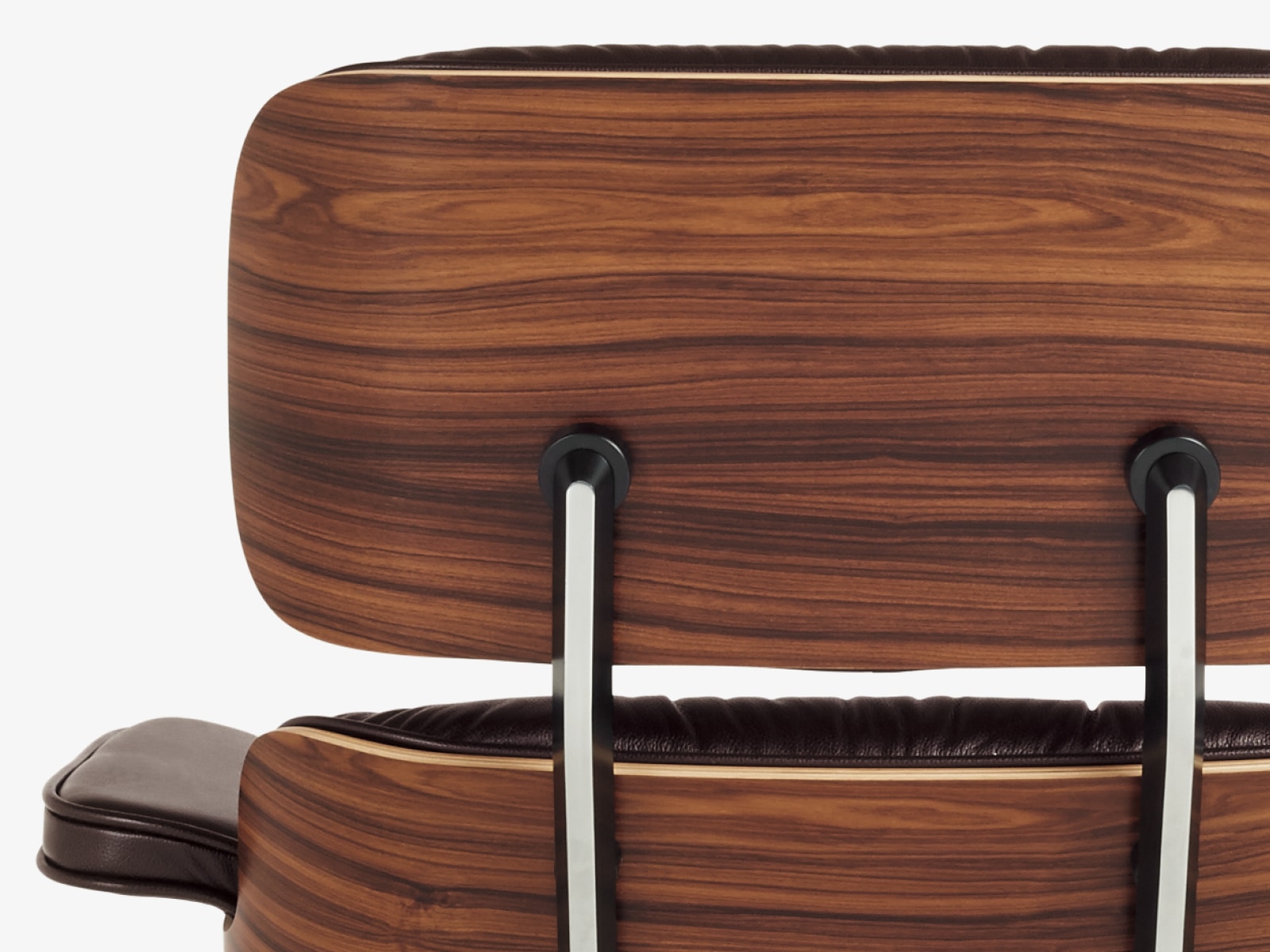 Close-up of the back of an Eames Lounge Chair with a wood veneer shell and black leather. Close-up of the back of an Eames Lounge Chair with a wood veneer shell and black leather.