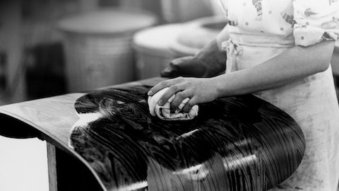 Close view of a hand applying the finish to the shell of an Eames Lounge Chair. Close view of a hand applying the finish to the shell of an Eames Lounge Chair.