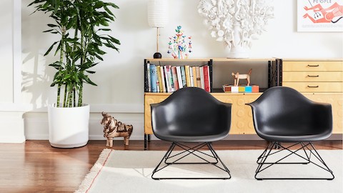 Two Eames Molded Plastic Armchairs with low wire bases on a rug in a living room setting. Two Eames Molded Plastic Armchairs with low wire bases on a rug in a living room setting.