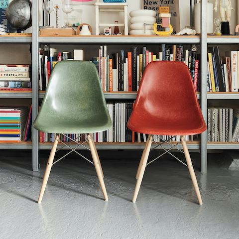 Two Eames Molded Fiberglass Side Chairs sitting in front of a bookshelf. Two Eames Molded Fiberglass Side Chairs sitting in front of a bookshelf.
