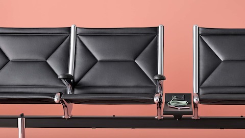 Three connected black sling seats with integrated power source on the table that includes USB-C port, USB-A port, and AC power outlet. Three connected black sling seats with integrated power source on the table that includes USB-C port, USB-A port, and AC power outlet.
