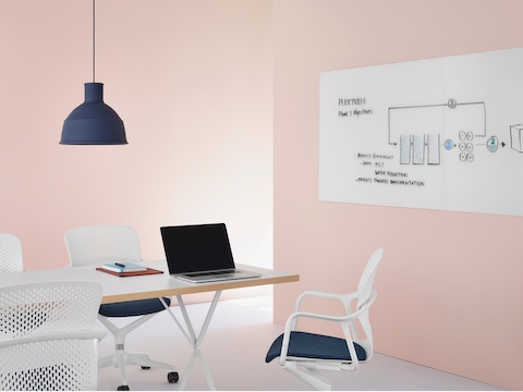 White Keyn Chairs with dark blue upholstery in a meeting space with a Glass White Board with brainstorming sketches on it at the end of a table. White Keyn Chairs with dark blue upholstery in a meeting space with a Glass White Board with brainstorming sketches on it at the end of a table.
