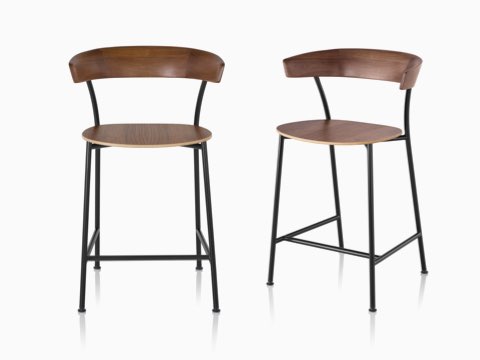 Two Leeway Stools with black metal bases and dark brown wood seats and backrests, one viewed from the front, the other viewed from an angle. Two Leeway Stools with black metal bases and dark brown wood seats and backrests, one viewed from the front, the other viewed from an angle.