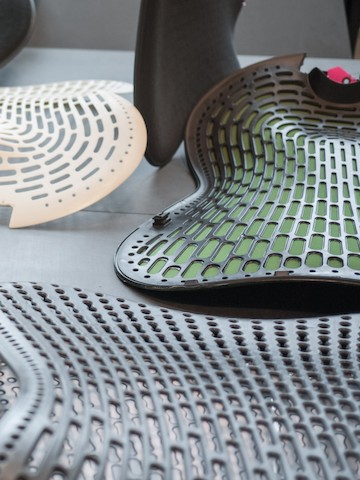 A detail view of parts of a Mirra 2 chair back construction. Several pieces of back and lumbar parts are arranged on a surface. A detail view of parts of a Mirra 2 chair back construction. Several pieces of back and lumbar parts are arranged on a surface.