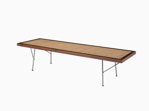 A Nelson Cane Bench with a walnut frame and metal legs, viewed from the side at an angle. A Nelson Cane Bench with a walnut frame and metal legs, viewed from the side at an angle.