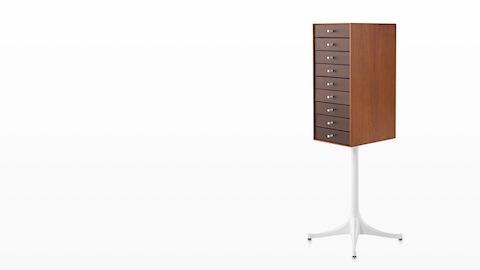 Angled view of a vertical nine-drawer Nelson Miniature Chest with a medium finish and white pedestal base. Angled view of a vertical nine-drawer Nelson Miniature Chest with a medium finish and white pedestal base.