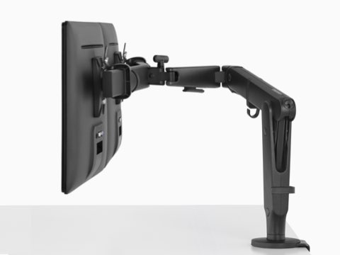 A side view of two monitors suspended above a white work surface from a black Ollin Monitor Arm. A side view of two monitors suspended above a white work surface from a black Ollin Monitor Arm.