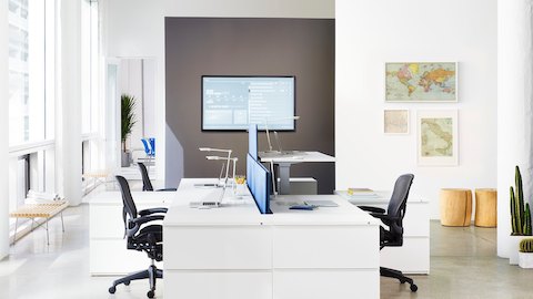 A Renew Sit-to-Stand Table integrated into a cluster of four workpoints with black Aeron office chairs. A Renew Sit-to-Stand Table integrated into a cluster of four workpoints with black Aeron office chairs.