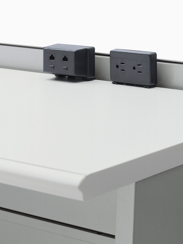 A Connect Voice/Data Outlet and a Connect two-outlet Electrical Distributor, both attached to the back of a work surface. A Connect Voice/Data Outlet and a Connect two-outlet Electrical Distributor, both attached to the back of a work surface.