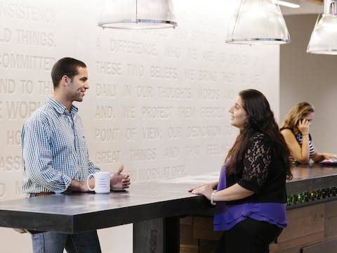 Two people converse at a high-top table while another talks on a phone. Two people converse at a high-top table while another talks on a phone.