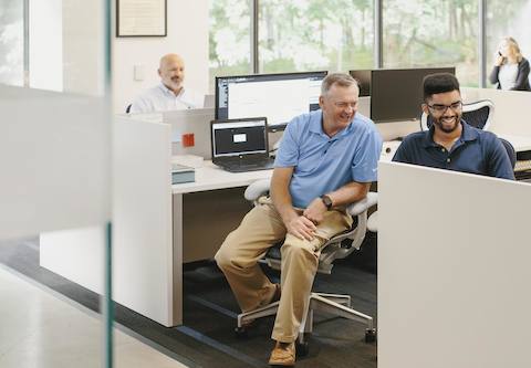 People sit at their computers inside of an open work space area. People sit at their computers inside of an open work space area.