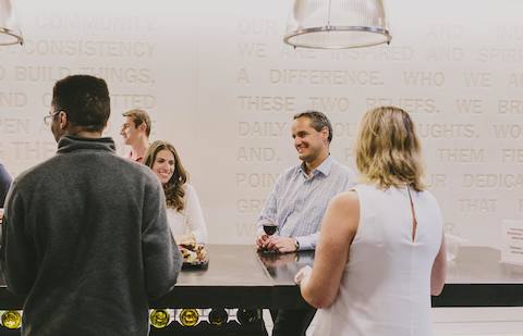People stand and drink wine at a high-top table. People stand and drink wine at a high-top table.
