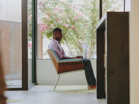 A man sits in a Swoop lounge chair while looking at his laptop. A man sits in a Swoop lounge chair while looking at his laptop.