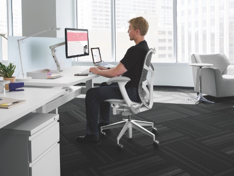 A man works at his computer while seated in a Mirra chair. A man works at his computer while seated in a Mirra chair.