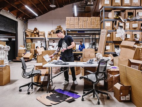 A man sorts through products at a desk inside of a warehouse area. A man sorts through products at a desk inside of a warehouse area.