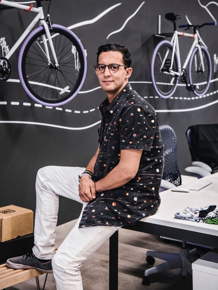 A man sits on a desk, with bicycles as decor on the wall behind him. A man sits on a desk, with bicycles as decor on the wall behind him.