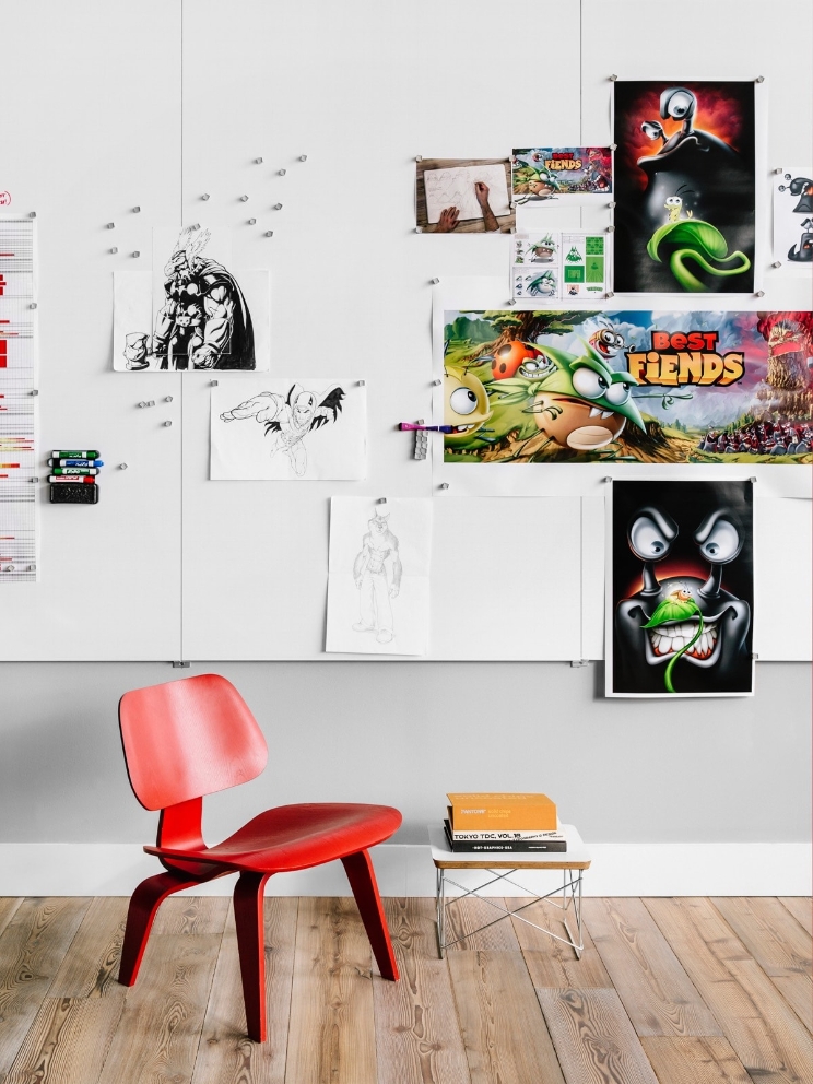 An office wall full of sketches and various illustrations behind a wood chair. An office wall full of sketches and various illustrations behind a wood chair.