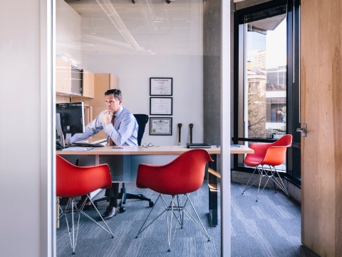 A man works at his office computer with three Eames molded chairs nearby. A man works at his office computer with three Eames molded chairs nearby.