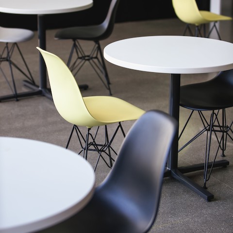 A close crop of three circular white-topped Everywhere Tables surrounded by yellow and black Eames Molded Plastic Shell Chairs. A close crop of three circular white-topped Everywhere Tables surrounded by yellow and black Eames Molded Plastic Shell Chairs.