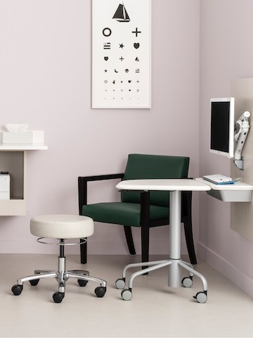 An exam room with Intent Solution wall unit holding a monitor on a Flo monitor arm and a mobile height adjustable table, with a Physician Stool, and a lounge chair. An exam room with Intent Solution wall unit holding a monitor on a Flo monitor arm and a mobile height adjustable table, with a Physician Stool, and a lounge chair.