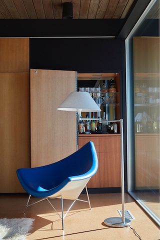 Sunshine pours in through a window of Craig Ellwood's Hunt House, bathing wood-paneled room featuring a blue Nelson Coconut Lounge Chair. Sunshine pours in through a window of Craig Ellwood's Hunt House, bathing wood-paneled room featuring a blue Nelson Coconut Lounge Chair.