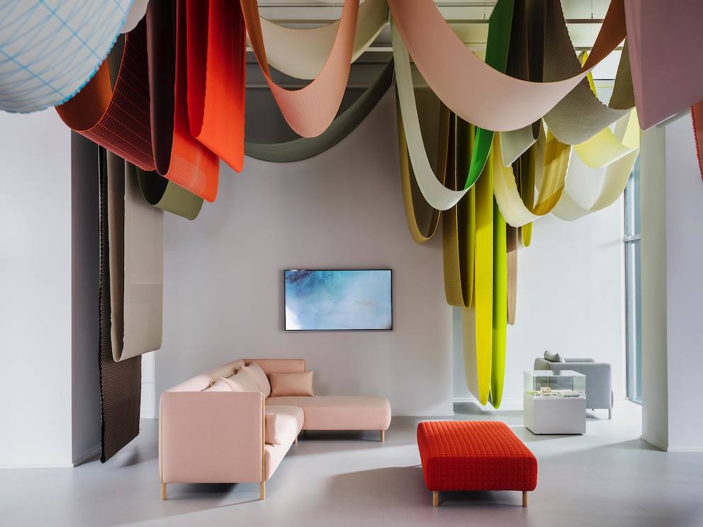 A pink ColourForm sectional and a red ColourForm ottoman beneath hanging textiles of various colors. A pink ColourForm sectional and a red ColourForm ottoman beneath hanging textiles of various colors.