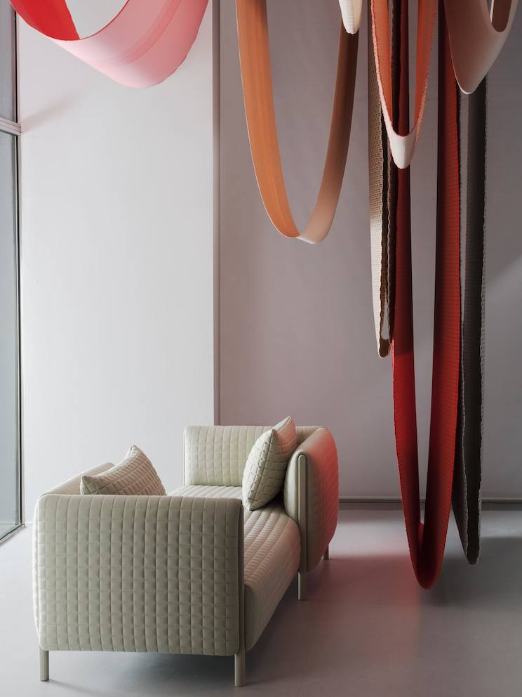 A ColourForm tête-à-tête sofa beneath hanging textiles of various colors. A ColourForm tête-à-tête sofa beneath hanging textiles of various colors.