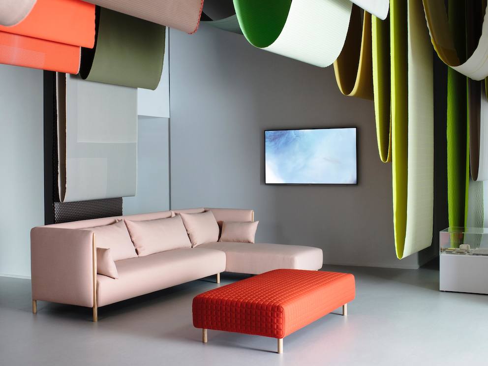 A pink ColourForm sectional and a red ColourForm ottoman beneath hanging textiles of various colors. A pink ColourForm sectional and a red ColourForm ottoman beneath hanging textiles of various colors.