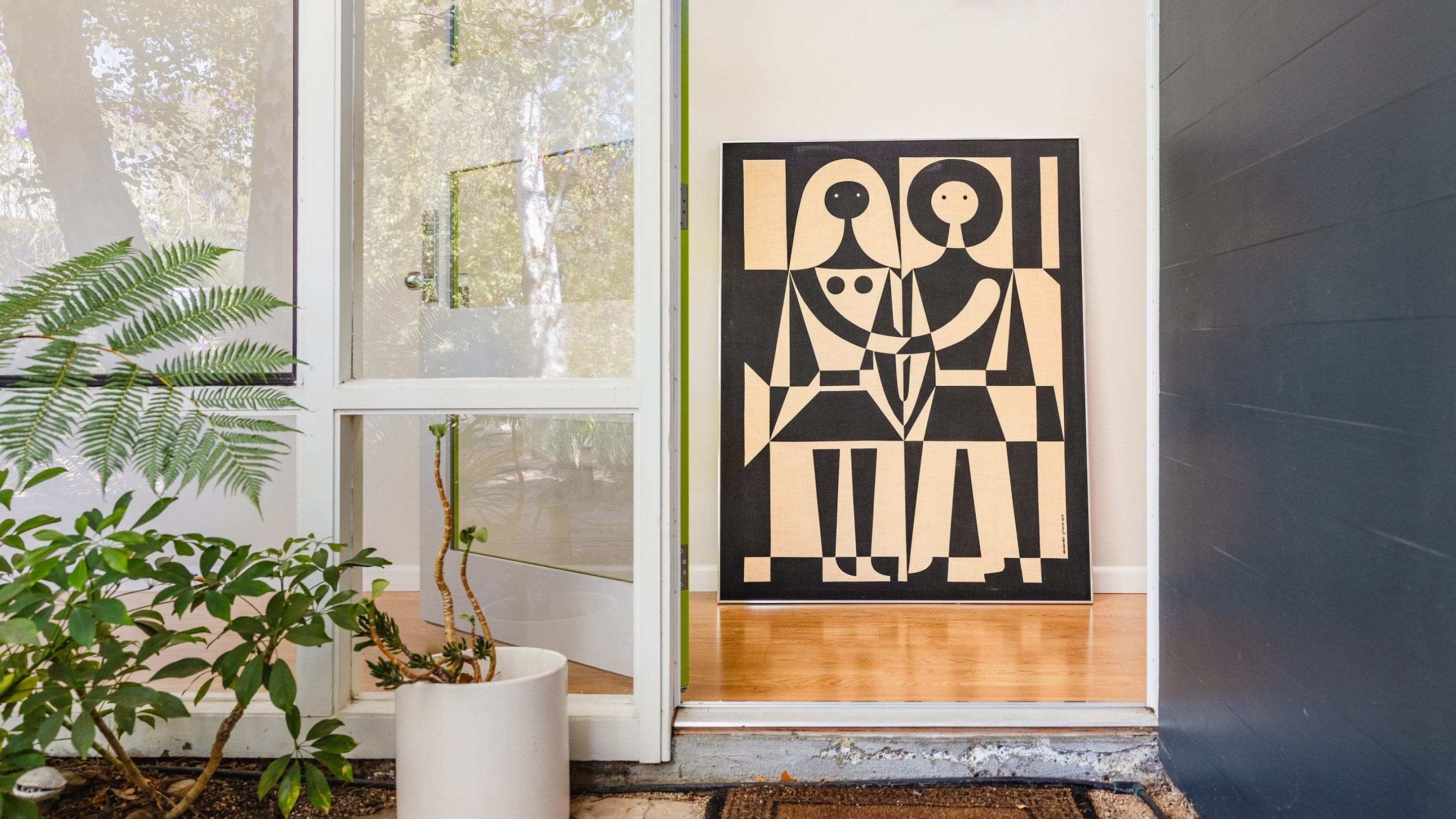 A bold black and white textile graphic of a man and woman is framed through modern windows and plants. A bold black and white textile graphic of a man and woman is framed through modern windows and plants.