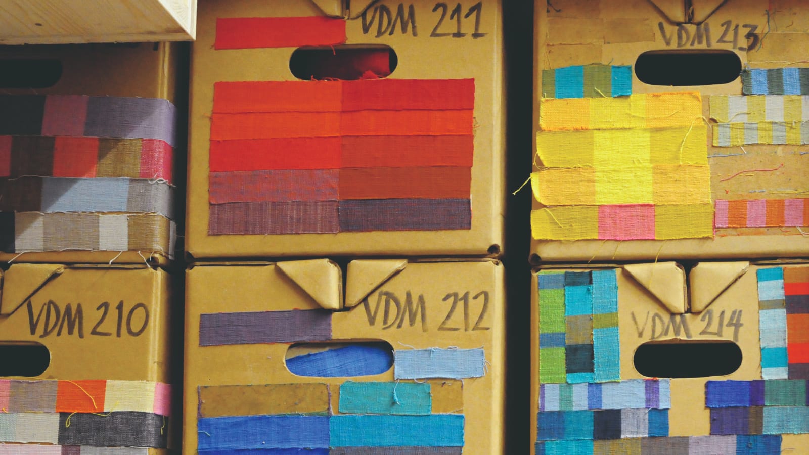 Detail shot of cardboard boxes stacked with colorful swatches taped to them. Detail shot of cardboard boxes stacked with colorful swatches taped to them.