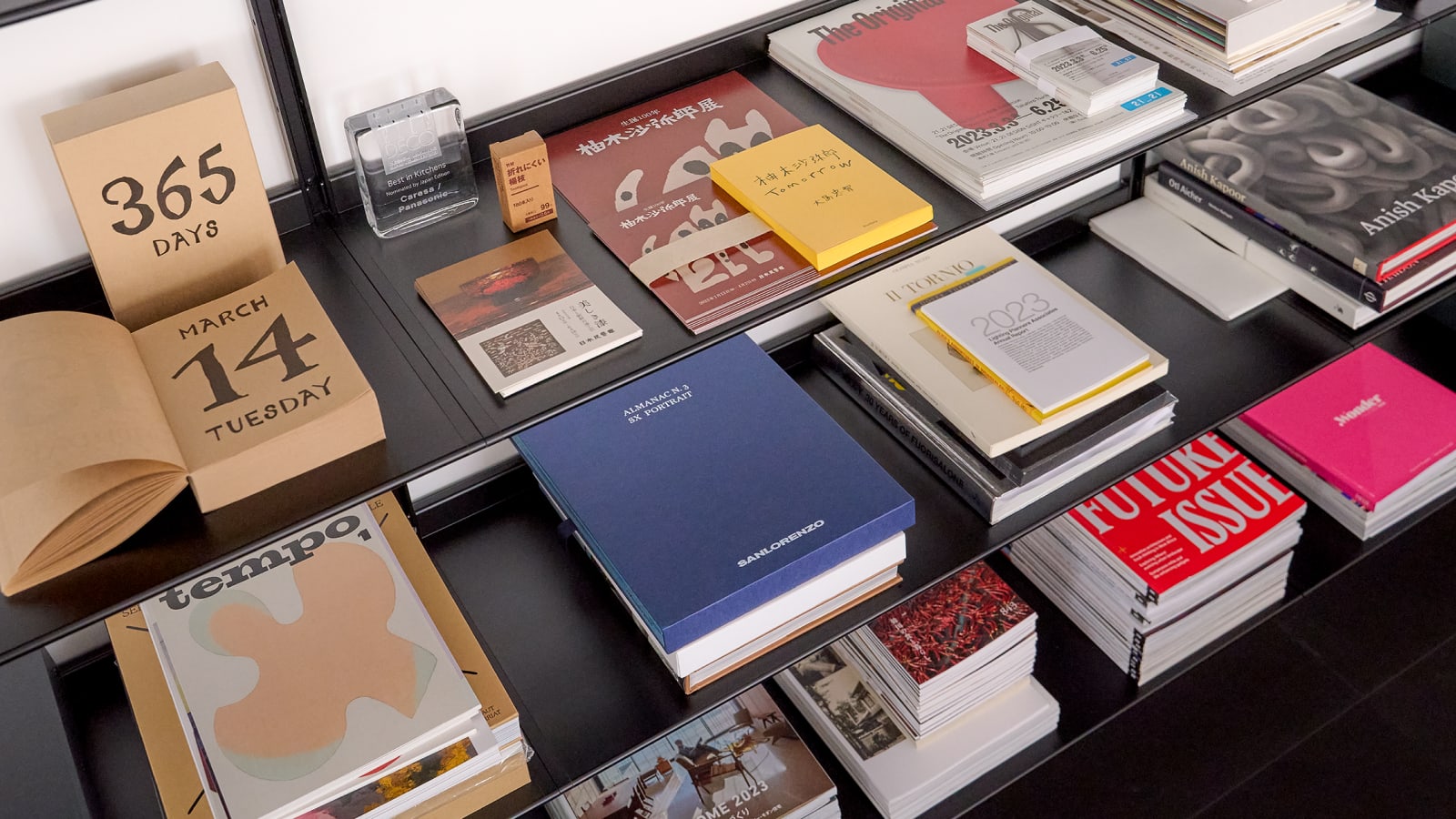 Various pieces of paper, books, and a calendar sit neatly stacked on a black shelf. Various pieces of paper, books, and a calendar sit neatly stacked on a black shelf.